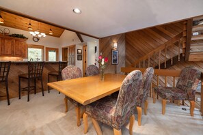 Ein Essbereich mit Holztisch und gemusterten Stühlen, eine Küche mit Holzschränken und eine Treppe mit Holzbalken.