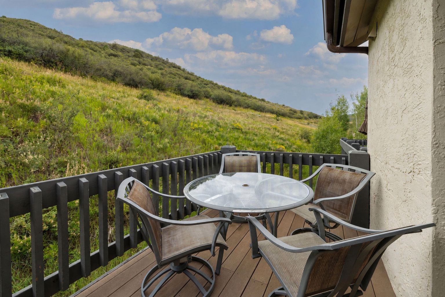An outdoor patio with a round table and four chairs, surrounded by a wooden deck and a black railing.