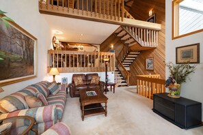 Un vaste espace de vie agrémenté d’un grand escalier en bois, d’un ensemble de canapés, d’une table basse et d’un buffet.