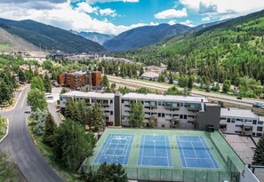 Ein Tennisplatz, umgeben von Gebäuden, einer Straße und einer Berglandschaft.