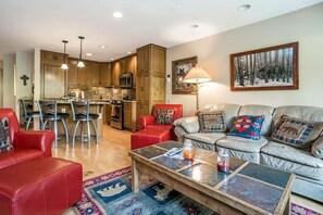 A living room with a sofa, a coffee table, and a kitchen area with wooden cabinets and a dining table. - Vail Simba Run 2 BR Condo with Resort Facilities (Vail)