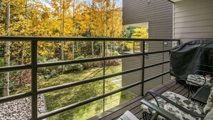 Un balcon donnant sur un jardin et des arbres, avec un barbecue et du mobilier d’extérieur.