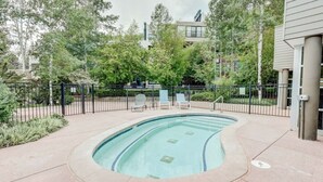 Une piscine à bord incurvé, entourée d’une clôture, avec des arbres en arrière-plan.