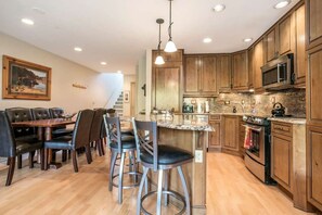 A modern kitchen with wooden cabinets, a central island with bar stools, and a dining area with a table and chairs. - Vail Simba Run 2 BR Condo with Resort Facilities (Vail)