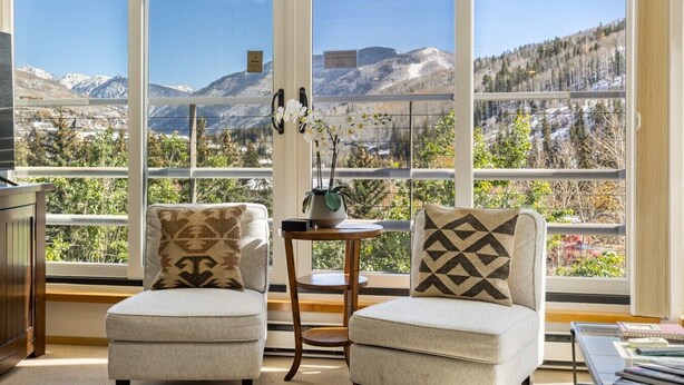 Una habitación con dos sillones, una mesita y vistas a montañas a través de amplios ventanales.