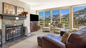 Una sala de estar con chimenea, televisión y grandes ventanales con vistas a un paisaje montañoso.