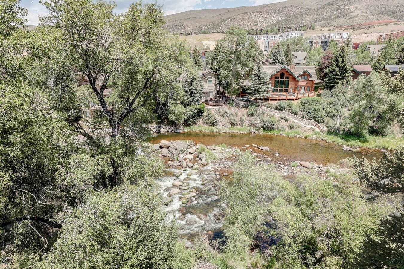 Un chalet offrant une vue sur une rivière sinueuse, entouré d’une forêt dense et bordé de collines.