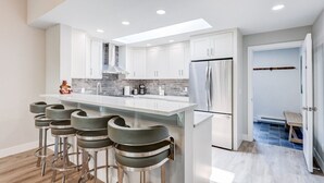 Une cuisine moderne avec des meubles blancs, un réfrigérateur en acier inoxydable et un coin bar avec des tabourets.