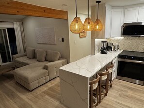 Una cocina moderna con una isla de mármol, taburetes de bar, horno empotrado y una zona de comedor con sofá.
