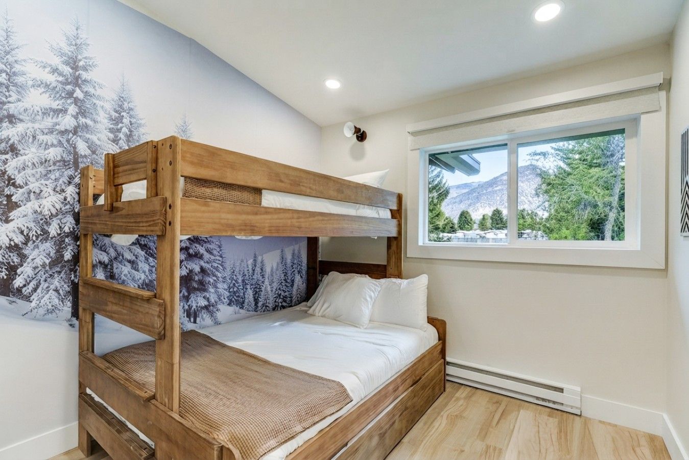Una cama individual sobre otra con un mural de bosque invernal, una ventana con vista a la montaña y una lámpara en el techo.