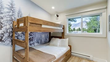 Una cama individual sobre otra con un mural de bosque invernal, una ventana con vista a la montaña y una lámpara en el techo.