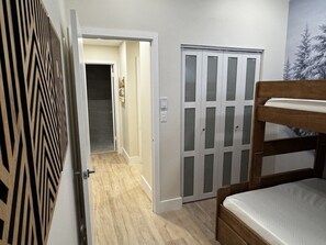 Un dormitorio con literas, un armario con puertas de vidrio esmerilado y un pasillo que conduce a otra habitación.
