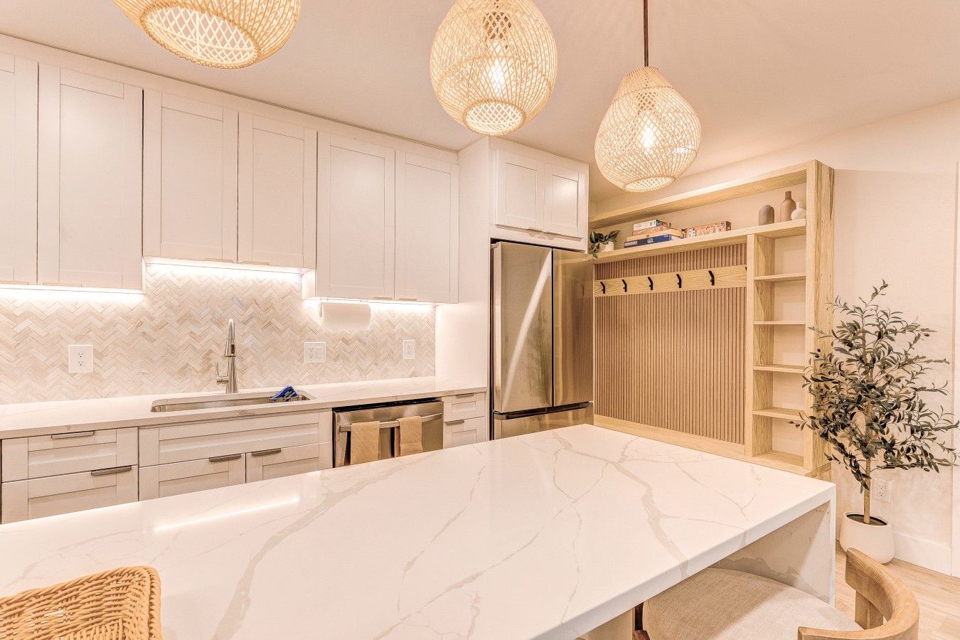 Una cocina moderna con armarios blancos, encimera de mármol y refrigerador integrado.