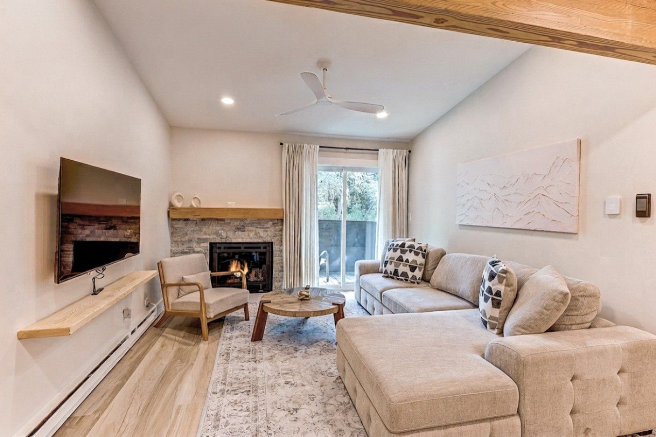 A modern living room with a flat-screen TV, a fireplace, a sofa, and a ceiling fan.