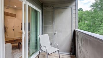 Un balcón con una silla, puerta corrediza de vidrio y vista a la vegetación.