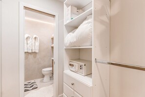Un baño con inodoro, perchero, microondas y una repisa con una caja.
