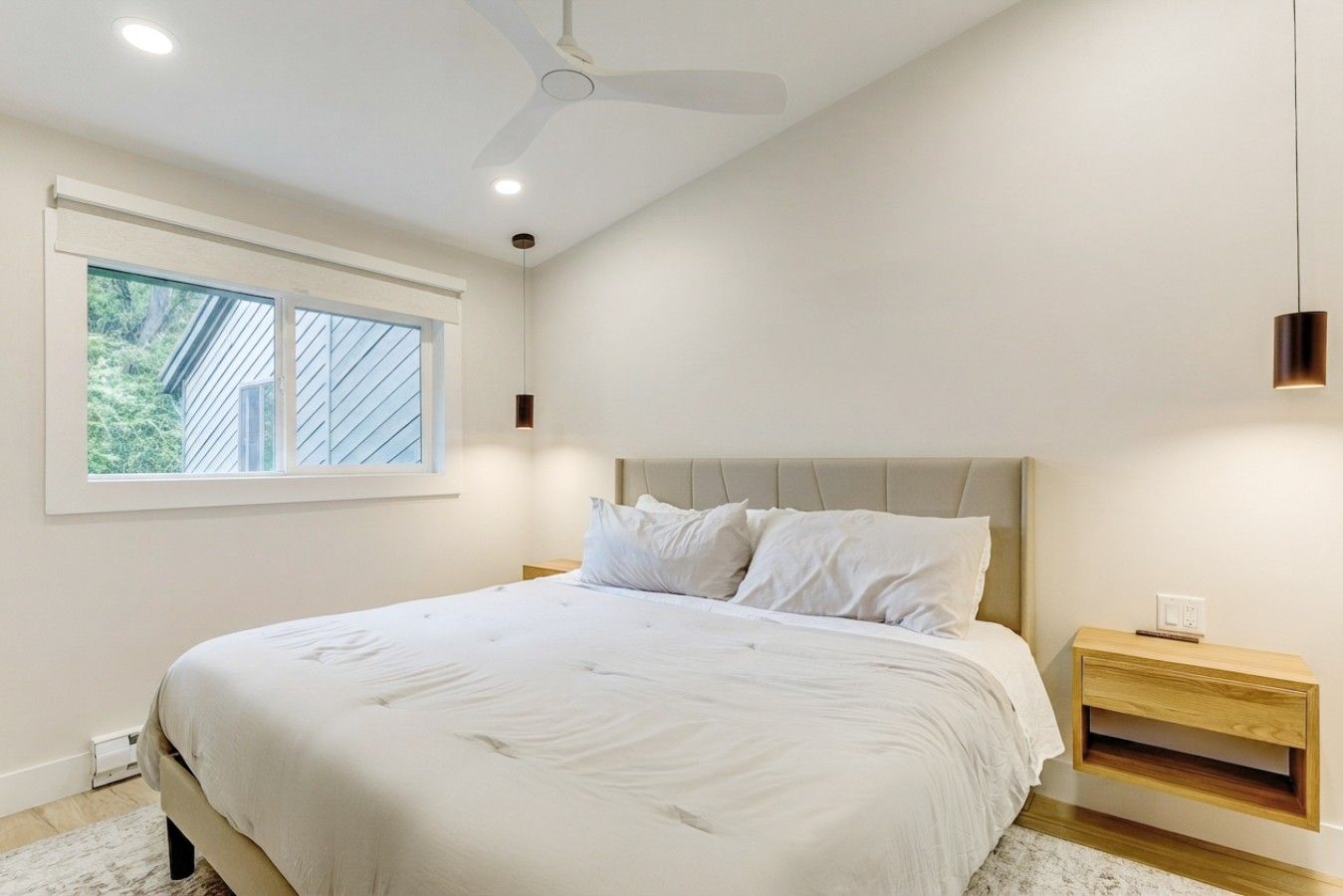 Un dormitorio con cama, mesita de noche, ventilador de techo y ventana.