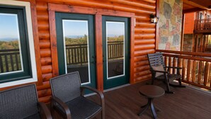 Una cabaña de madera con terraza, dos puertas con paneles de vidrio y un muro de piedra.
