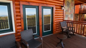 A wooden cabin with a deck, two doors with glass panels, and a stone wall. - Modern Luxury 4 Bedroom/4 Bathroom Cabin w/ AC + Free Access to Waterpark (Gatlinburg)