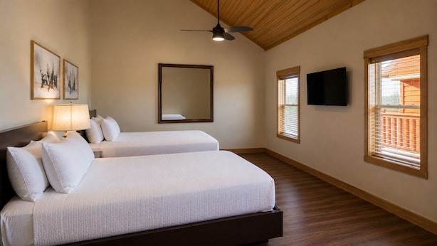 Un dormitorio con dos camas, ventilador de techo, televisor y ventana con persianas.