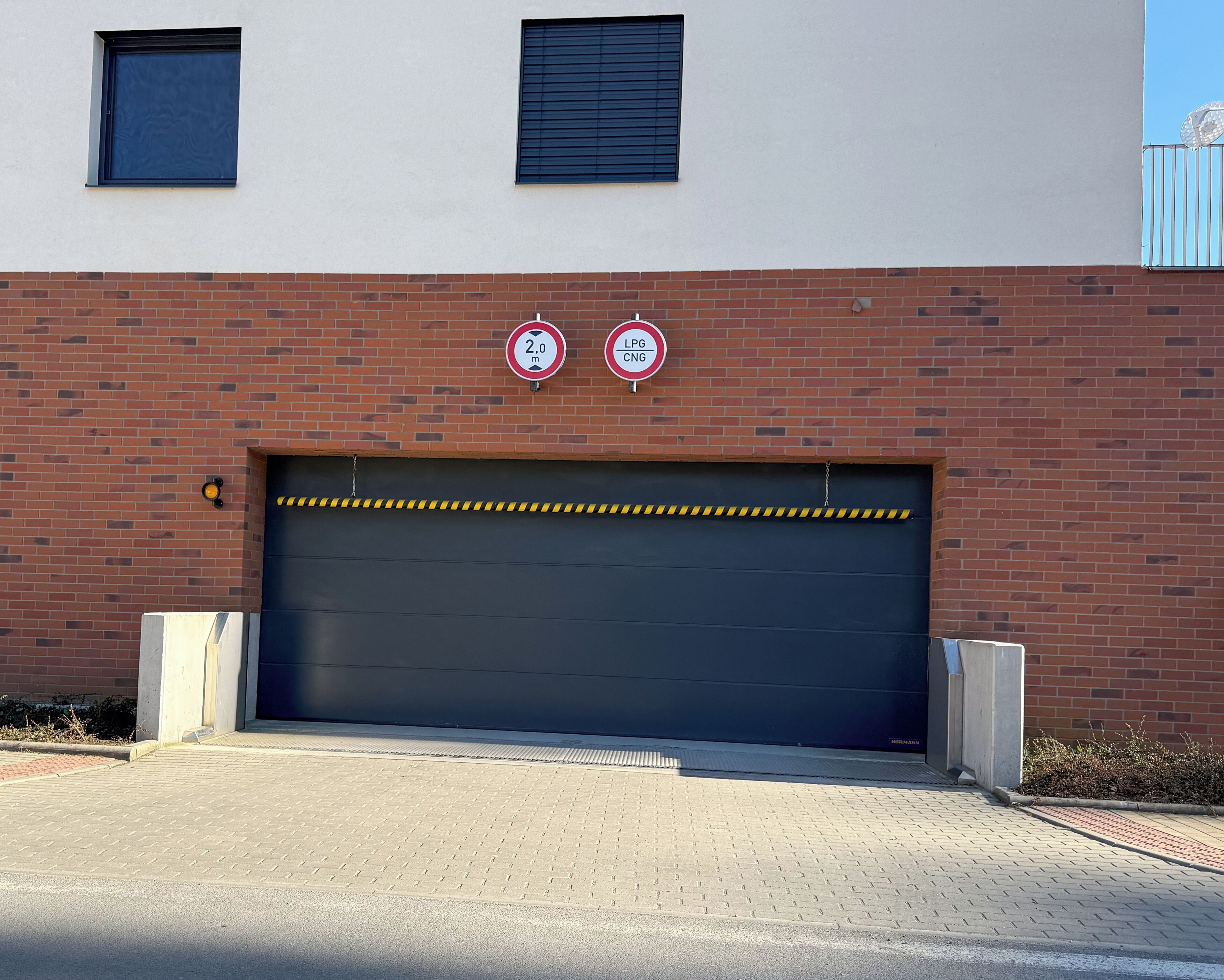 Un edificio con una puerta de garaje, dos carteles de 'prohibido estacionar' y cinta de precaución amarilla a través de la puerta.