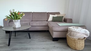 En moderne stue med en grå sofa, et rundt sofabord, en fletkurv og en vase med blomster.