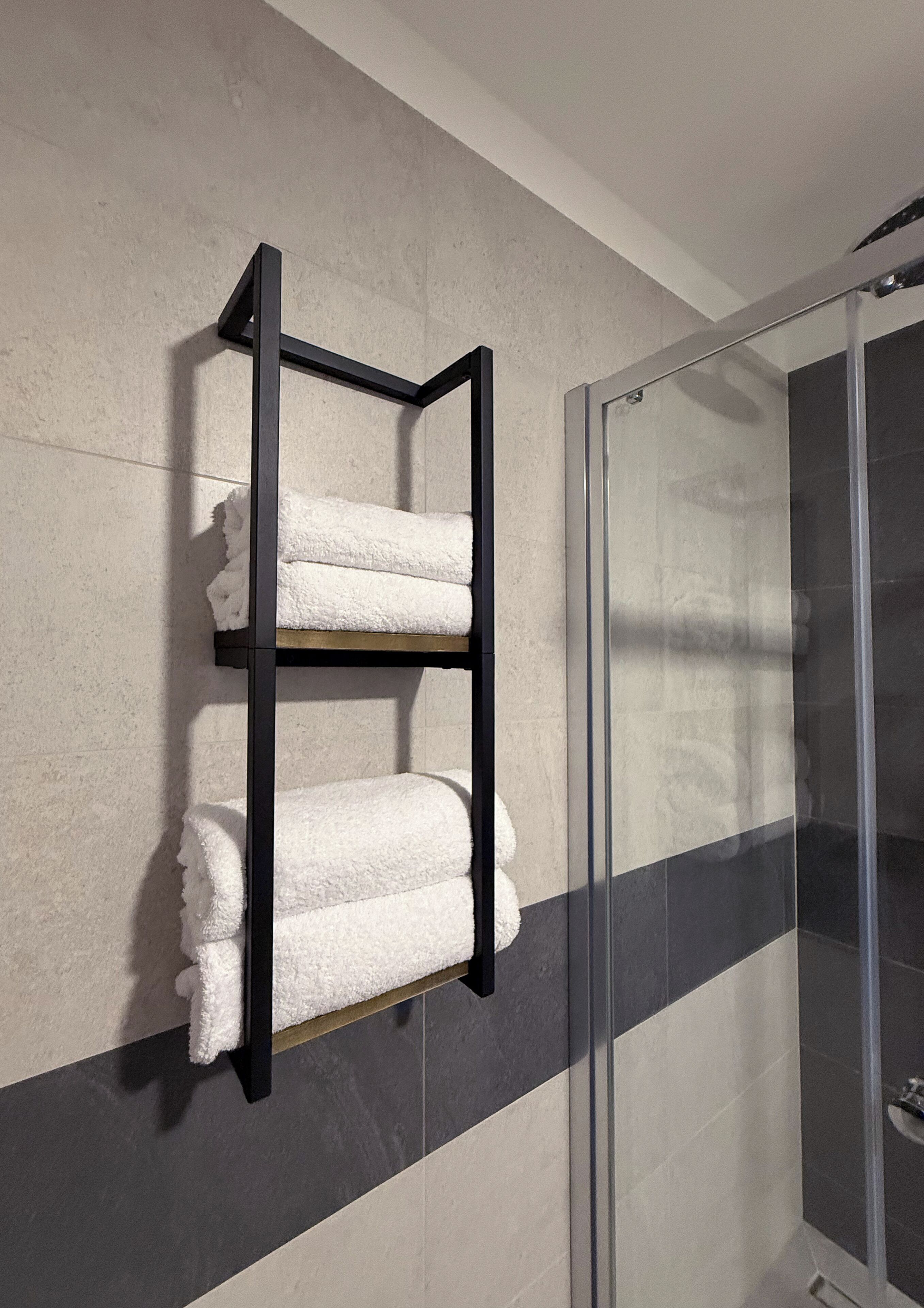 A bathroom with a towel rack holding two towels, a glass shower enclosure, and a tiled wall.