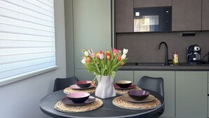 Een moderne eetruimte met een ronde tafel, zwarte stoelen, een vaas tulpen, en een keuken op de achtergrond.