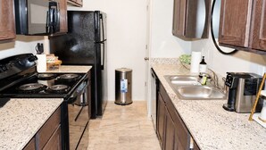 A compact kitchen with a stove, microwave, refrigerator, sink, and wooden cabinets. - Haven on the Hill, Modern 3BR Near Fort Cavazos (Copperas Cove)