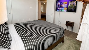 A bedroom with a bed, a TV mounted on the wall, a ceiling fan, and a door leading to another room. - Haven on the Hill, Modern 3BR Near Fort Cavazos (Copperas Cove)
