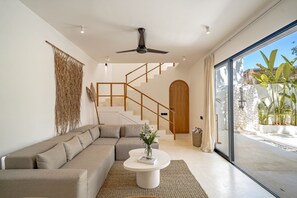 Ein modernes Wohnzimmer mit einer Eckcouch, einem Couchtisch, einem Deckenventilator und einer Holztreppe zu einer Holztür.
