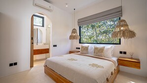 Une chambre avec un grand lit, une fenêtre donnant sur des arbres, une table de chevet avec une lampe et un appareil de climatisation.