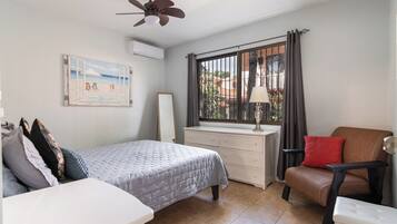 Une chambre à coucher comprenant un lit, un bureau, une chaise, un ventilateur de plafond et une fenêtre avec des rideaux.