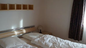A room with two beds, a wooden headboard, a bedside table with a lamp, and a window with curtains. - Dilaila, (Grächen), by Interhome (Grächen)