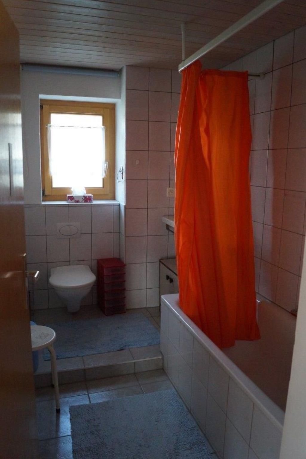 Un bagno piccolo con il water, una finestra, una tenda per la doccia e uno scalino che conduce a una vasca da bagno.