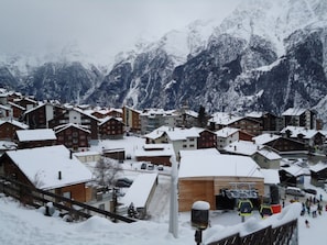 Ein verschneites Bergdorf mit Chalets, einer Seilbahn und einer Skipiste.
