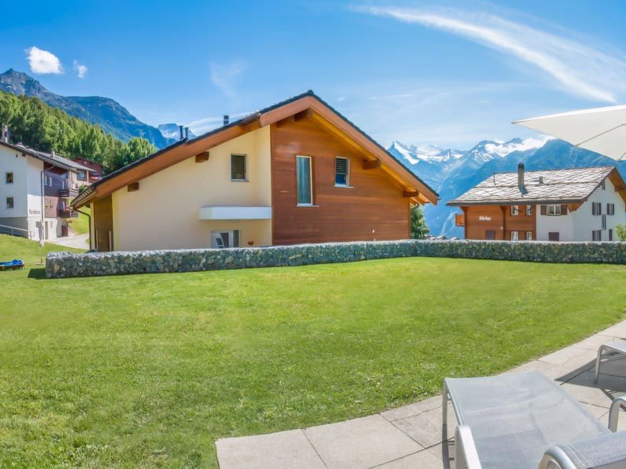 Un chalet en bois, doté de fondations en pierre, entouré d’une pelouse bien entretenue et avec une chaîne de montagnes en toile de fond.