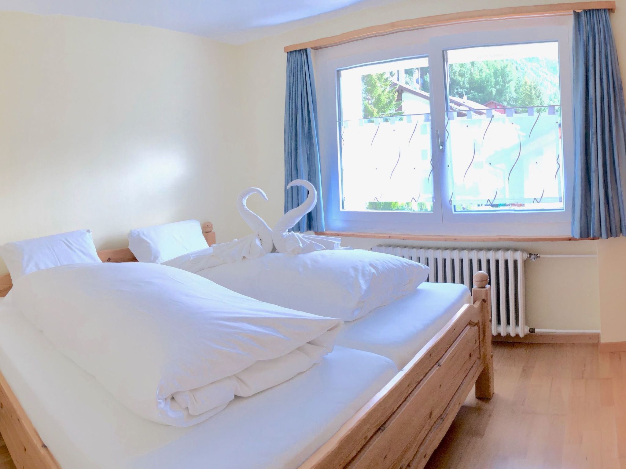 Un lit double avec du linge de lit blanc, dans une chambre dotée d’une fenêtre et de rideaux.