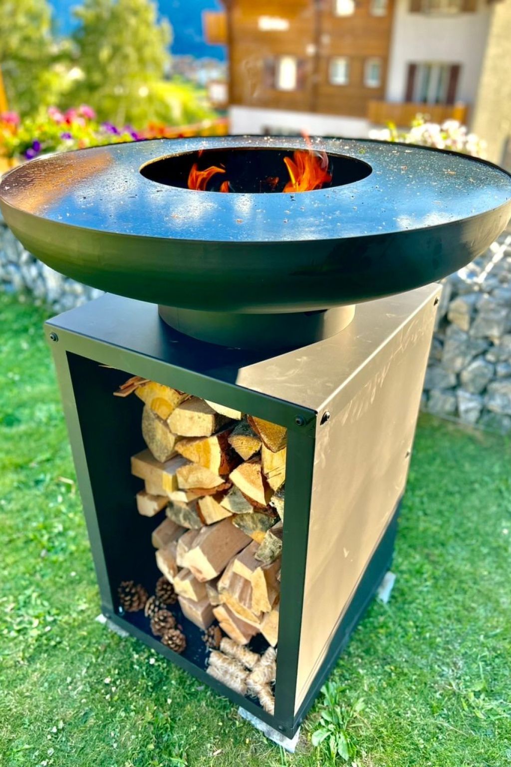 A metal outdoor fire pit with a circular top and a fire burning inside.