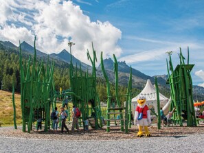 A mascot in a red and white costume standing in front of a green structure with people around. - Swiss, (Grächen), 1066 by Interhome (Grächen)
