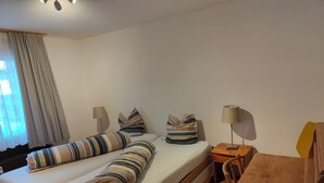 Una cama doble con ropa de cama a rayas, una mesita de noche con lámpara y una mesita auxiliar de madera.