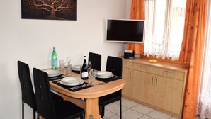 Ein Essbereich mit einem Tisch für vier Personen, Stühlen, einem Fernseher und einem fenster mit Vorhängen.