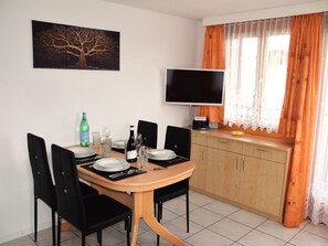 Ein Essbereich mit einem Tisch für vier Personen, Stühlen, einem Fernseher und einem fenster mit Vorhängen.