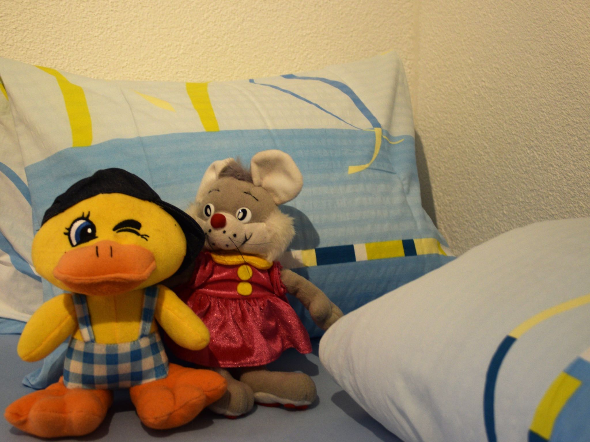 Two plush toys on a bed with a patterned pillow.