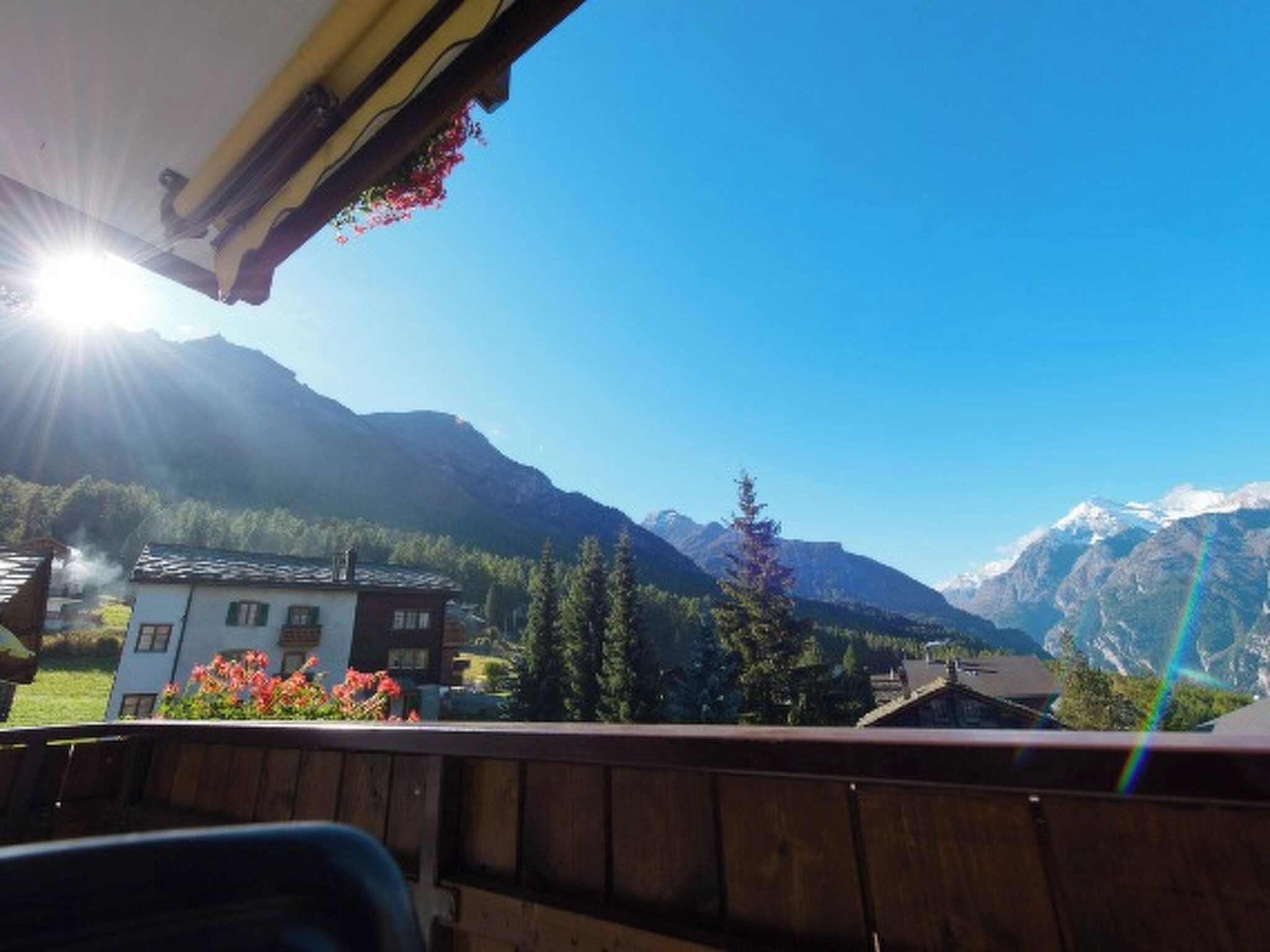Une vue sur les montagnes depuis un balcon doté d’une balustrade en bois, un ciel dégagé et une maison au premier plan.