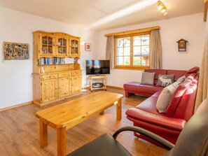 Een gezellige woonkamer met een houten salontafel, een rode bank, een televisie en een houten kast met glazen deuren.