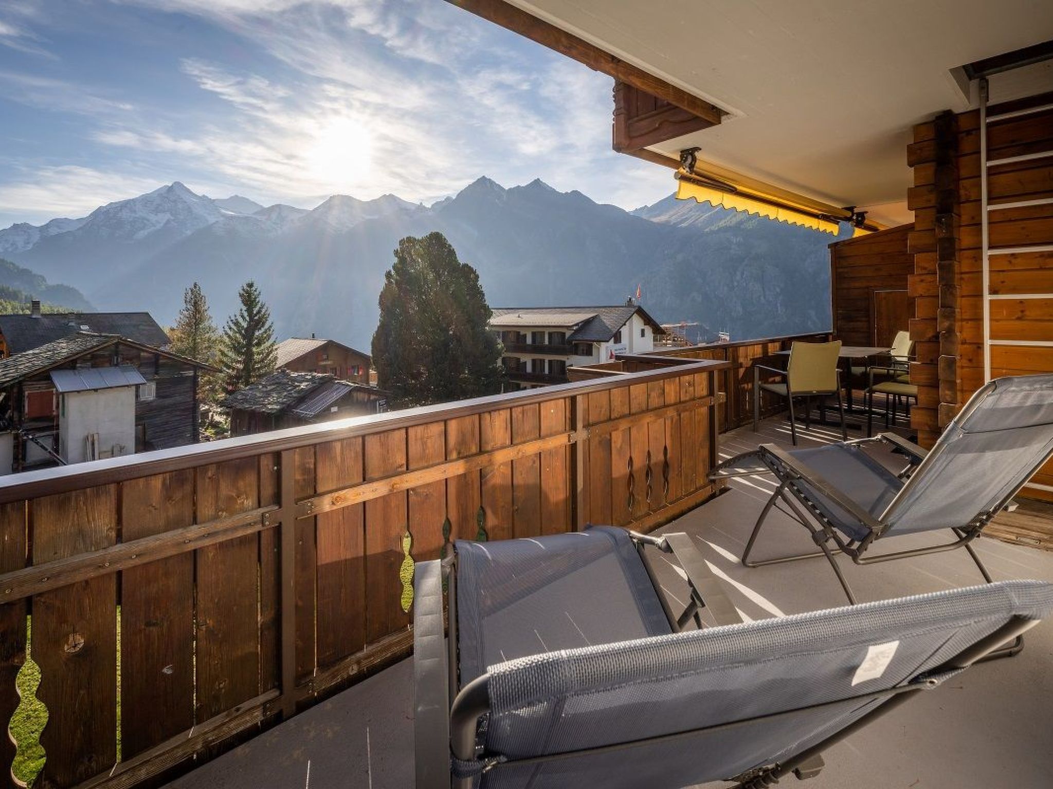 A balcony with wooden railings, two lounge chairs, and a view of mountains.