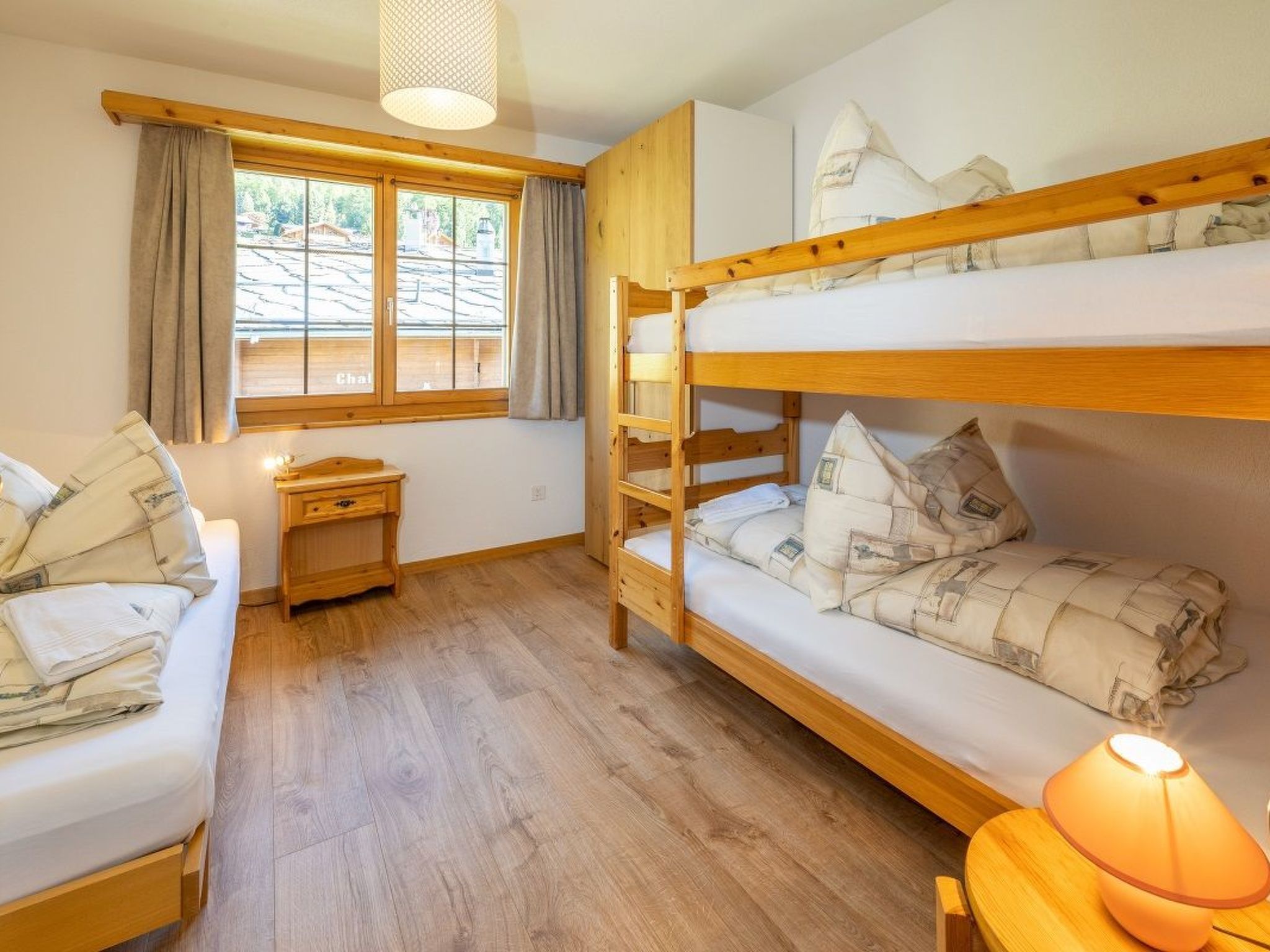 A bunk bed room with a window, a bedside table, and a lamp.