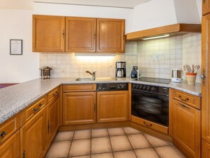 A kitchen with wooden cabinets, a built-in oven, a coffee maker, and a sink. - Anna 33, (Grächen), 1307 by Interhome (Grächen)