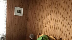 Ein Zimmer mit Holzwandverkleidung, zwei Betten mit grün-schwarzer Bettwäsche, einem gerahmten Bild an der Wand und einem Nachttisch mit Lampe.